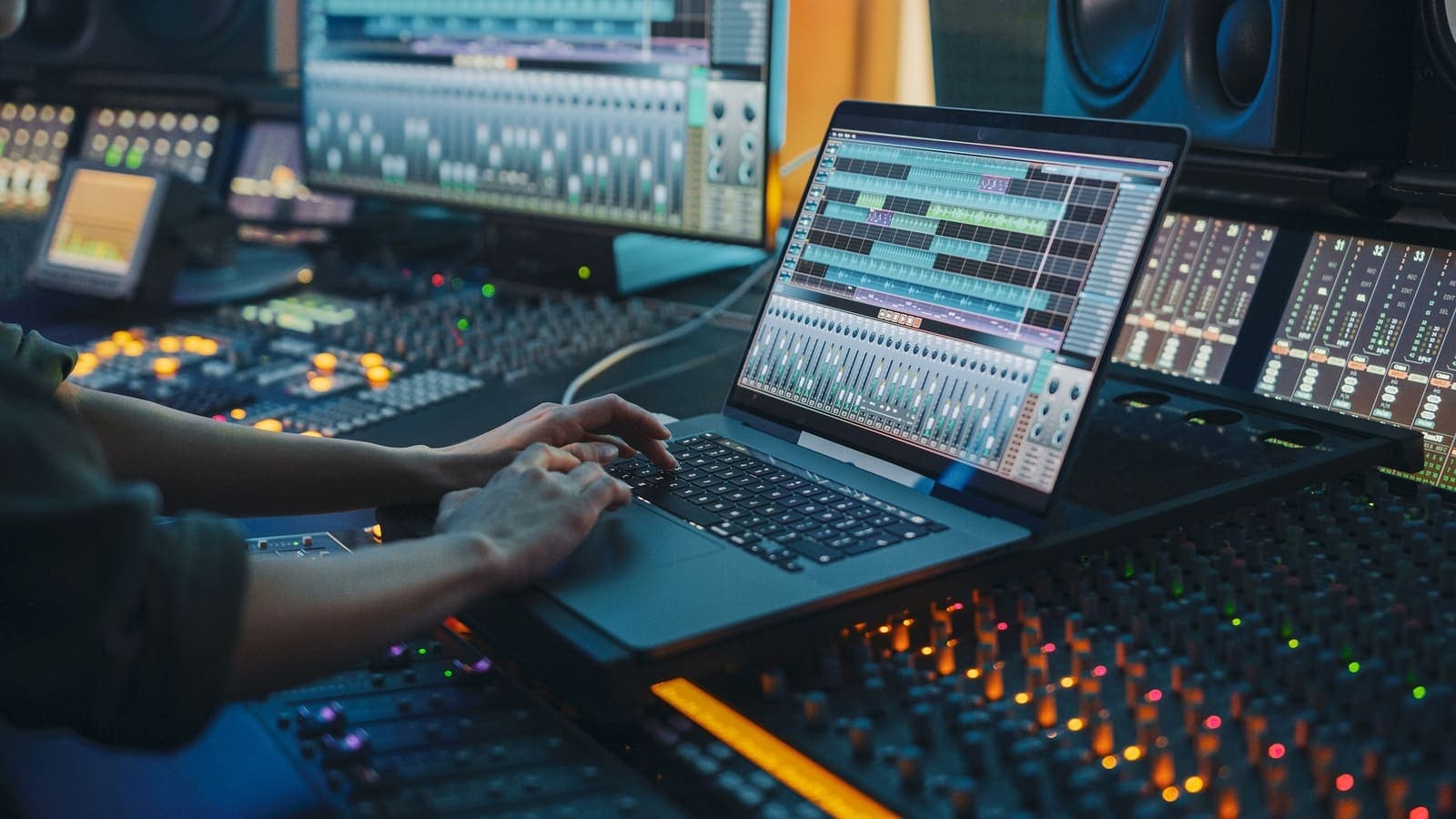 Hands typing on a laptop running a mixing session beside a studio console