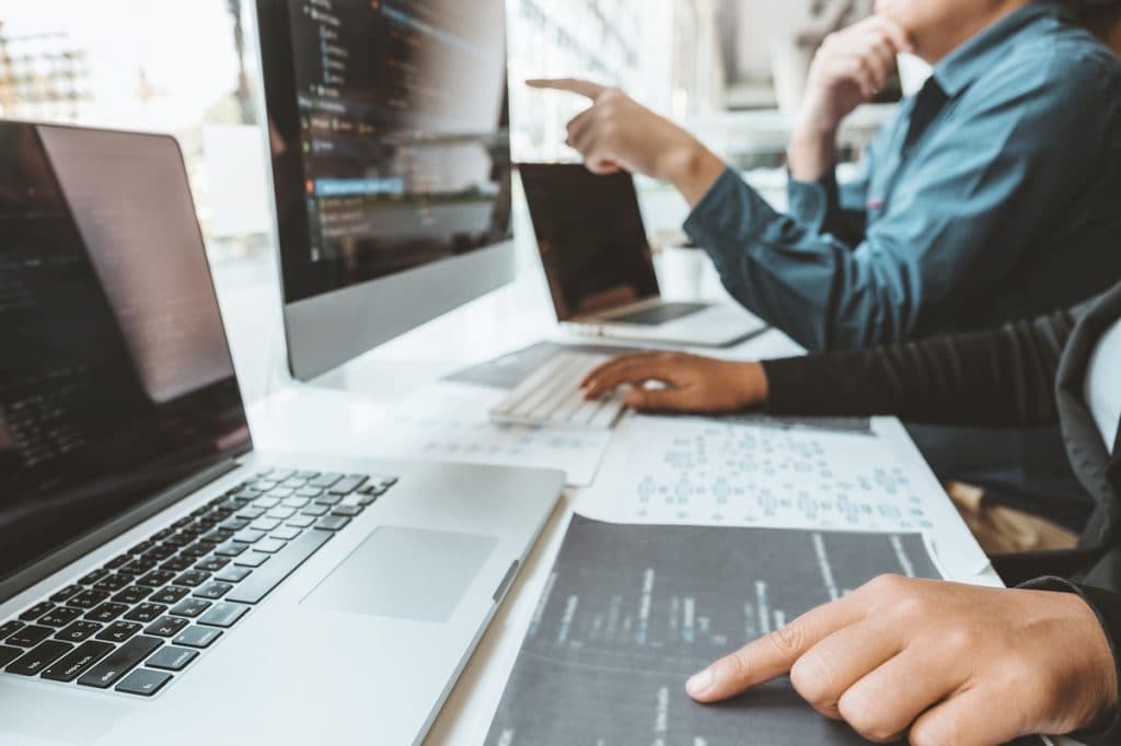 Two developers reviewing code together on a laptop and a desktop screen